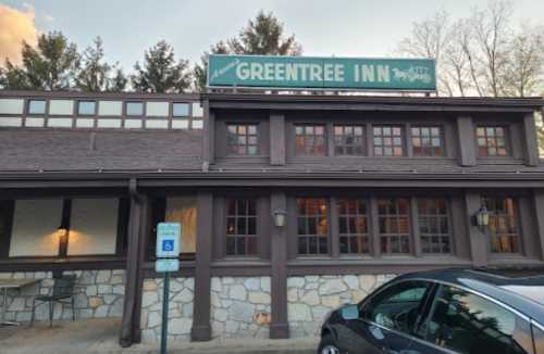 Exterior of Greentree Inn, featuring a wooden facade and large sign, with trees in the background and a parked car.