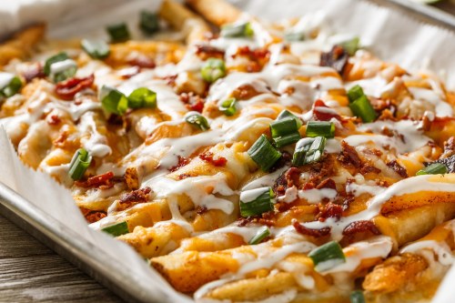 A tray of loaded fries topped with cheese, bacon, green onions, and drizzled with sour cream.