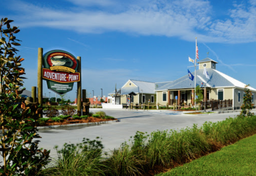 A building with a sign reading "Adventure Point" surrounded by greenery and a clear blue sky.