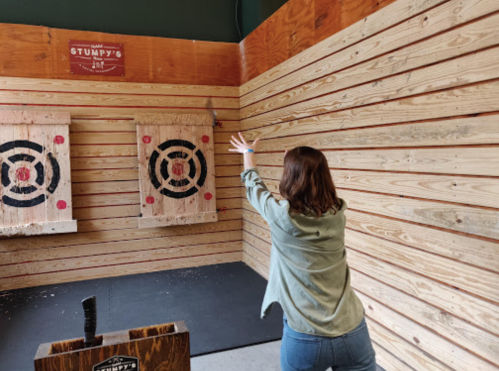 A person throwing an axe at a target in a wooden-walled axe-throwing venue.