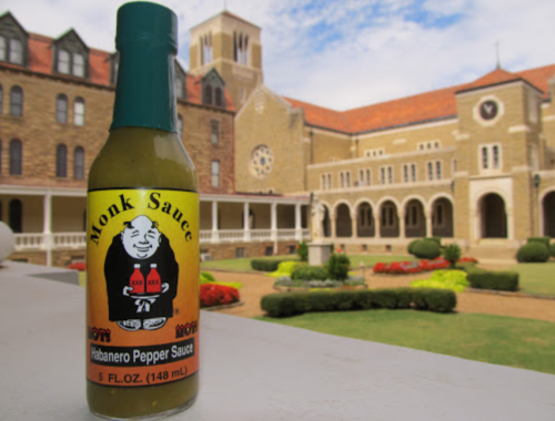 A bottle of Monk Sauce habanero pepper sauce in front of a historic building with gardens.