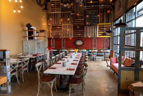 A cozy restaurant interior with wooden decor, a long table, and colorful seating against a rustic wall.
