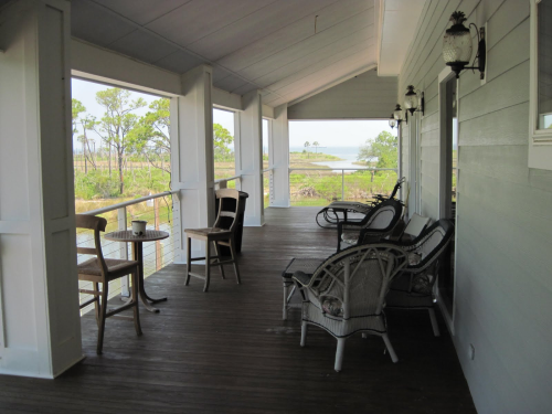 A spacious porch with wicker chairs and a small table, overlooking a scenic view of trees and water.