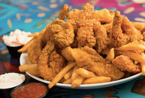 A large plate of golden fried shrimp and chicken, served with crispy fries and dipping sauces on the side.