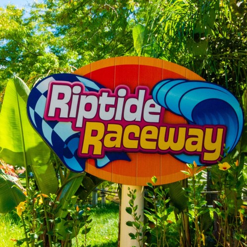 Colorful sign for "Riptide Raceway" surrounded by lush greenery and tropical plants.