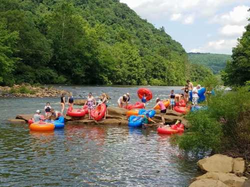 People enjoying a summer day on the river, floating on colorful inner tubes and relaxing on rocks surrounded by greenery.