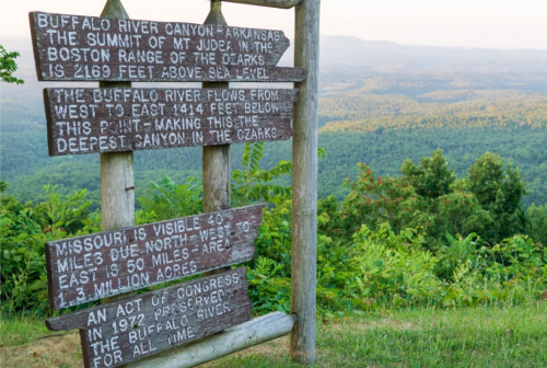 Wooden signpost with text about Buffalo River Canyon and Mt. Judea, overlooking a lush green landscape in the Ozarks.