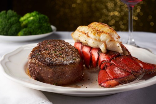 A gourmet plate featuring a juicy steak and lobster tail, garnished with herbs, alongside a side of broccoli.