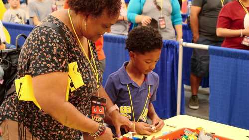 A woman and a child play with colorful building blocks at a crowded event, both wearing name tags.