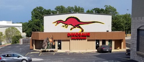 Exterior of a Dinosaur Museum featuring a large dinosaur mural and a dinosaur sculpture in front.