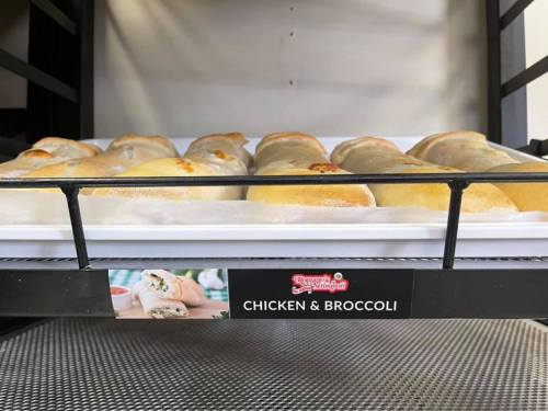 A display case filled with chicken and broccoli calzones on a white tray.