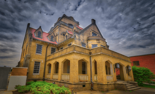 A historic, multi-story building with a unique architectural design, featuring a textured facade and cloudy sky.
