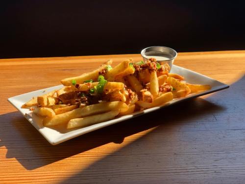 A plate of golden fries topped with green onions and served with a small dipping sauce on a wooden table.