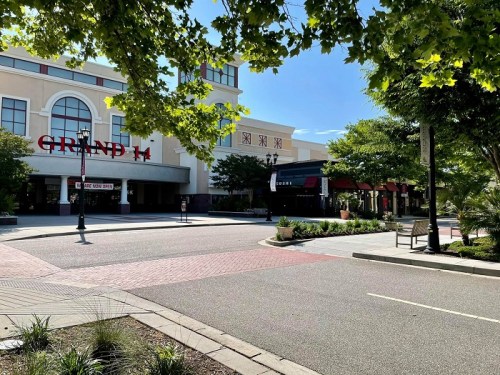 A sunny street view of a shopping area featuring the Grand 14 theater and surrounding greenery.