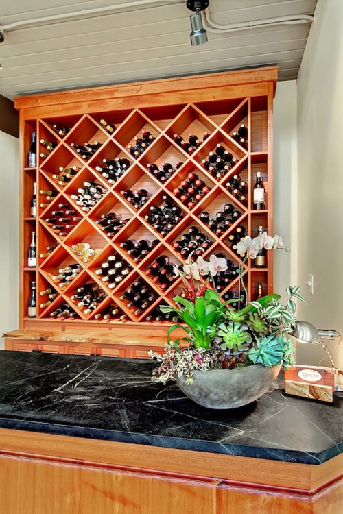 A wooden wine rack filled with various bottles, beside a dark countertop featuring a decorative plant arrangement.