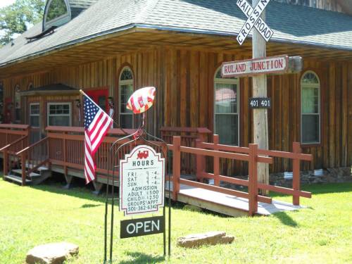 A wooden building with a sign reading "Ruland Junction," an American flag, and a balloon in front. Open hours displayed.
