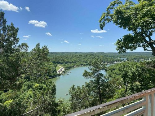 A scenic view of a river winding through lush green hills under a clear blue sky with a few clouds.