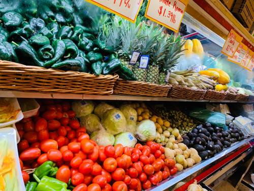 A vibrant display of fresh vegetables and fruits, including peppers, tomatoes, pineapples, and avocados in a market.