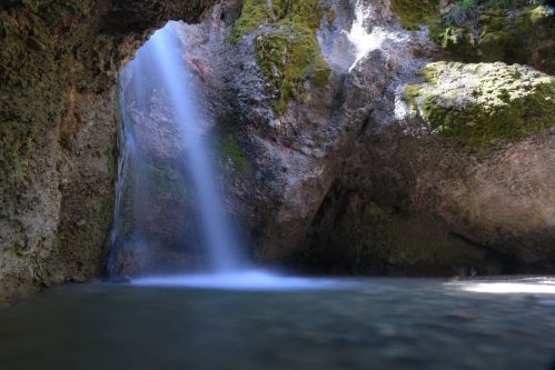 A serene waterfall cascades into a tranquil pool, surrounded by moss-covered rocks and lush greenery.