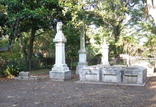 A quiet cemetery scene featuring several weathered gravestones surrounded by trees and a fence.