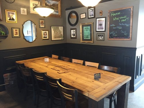 A cozy dining area with a large wooden table, framed pictures on the walls, and a chalkboard for suggestions.