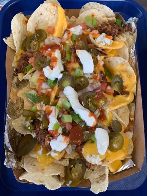 A tray of nachos topped with cheese, pulled meat, jalapeños, tomatoes, green onions, and sour cream.