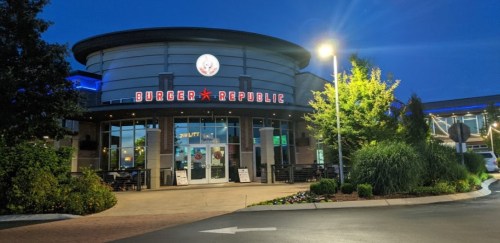 Exterior of Burger Republic restaurant at night, featuring bright signage and surrounding greenery.