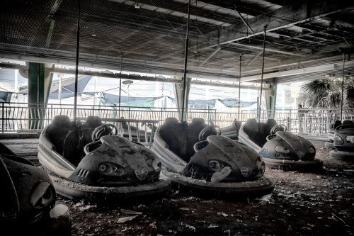 Abandoned bumper cars in a dusty, dimly lit amusement park, with debris scattered around and a sense of neglect.