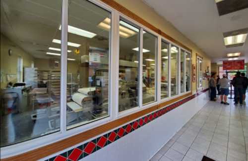 A view through large windows into a bakery kitchen, with people waiting in line outside.