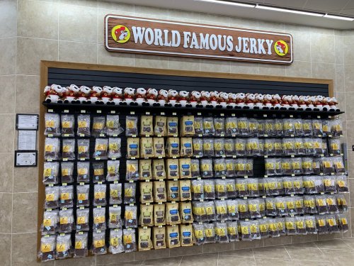 A wall display of various jerky packages at a store, topped with plush toys and a sign reading "World Famous Jerky."
