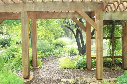 A wooden pergola frames a lush garden path surrounded by greenery and trees, creating a serene outdoor space.