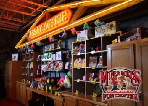 Brightly lit "Assay Office" display with shelves of toys and games at Miner Mike's Fun Center.
