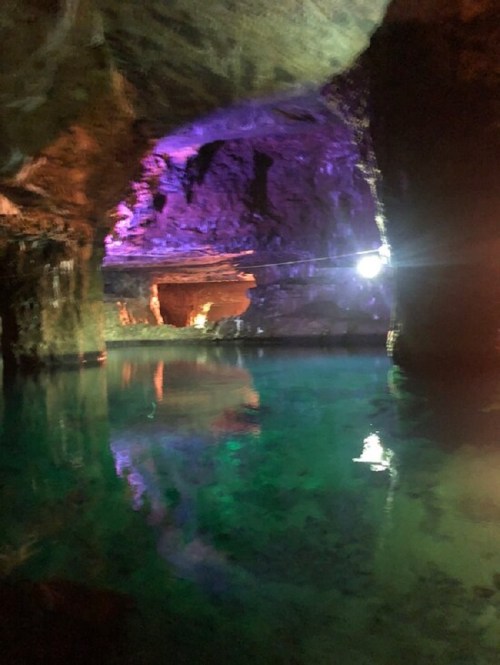 A dimly lit cave with colorful lights reflecting on still water, creating a serene and mystical atmosphere.