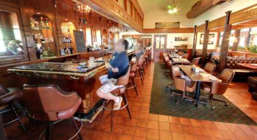 A cozy bar interior with wooden decor, empty tables, and a person sitting at the counter.