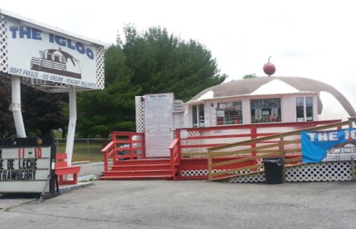 A colorful ice cream stand named "The Igloo," featuring a large cherry on top and a menu board outside.