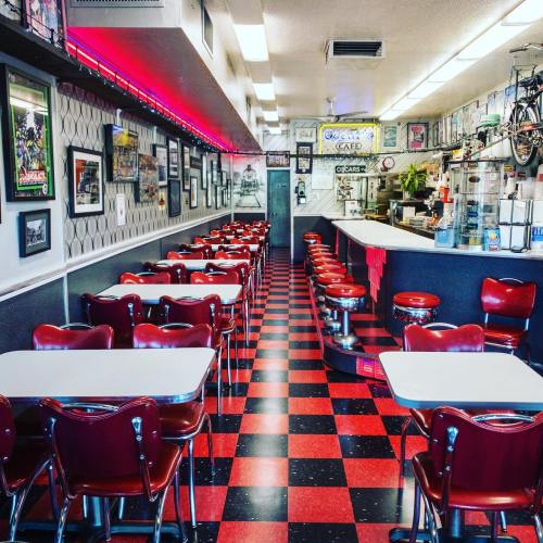 A retro diner interior with red and black checkered floors, red chairs, and vintage decor lining the walls.