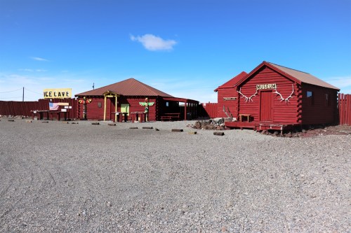 Two red wooden buildings in a gravel area, one labeled "Museum" and the other "Ice Cave," under a clear blue sky.