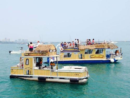 Two colorful boats with thatched roofs on a calm blue sea, filled with people enjoying a sunny day.
