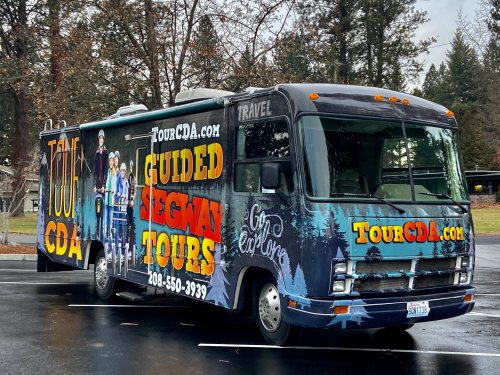 A colorful tour bus promoting guided Segway tours, parked in a wooded area with contact information displayed.