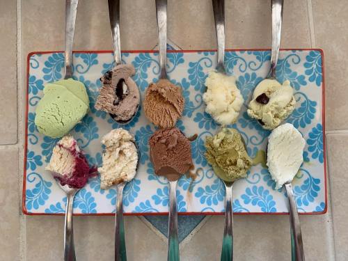 A colorful assortment of ice cream scoops on a decorative platter, each with a metal spoon.