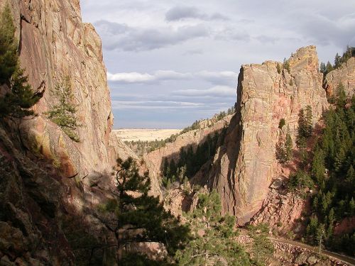 A scenic view of a narrow canyon with towering rock formations and lush trees under a cloudy sky.