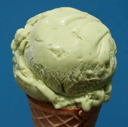A close-up of a green ice cream scoop on a waffle cone against a blue background.