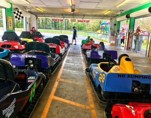 A row of colorful go-karts lined up in a garage, with people preparing to race in the background.