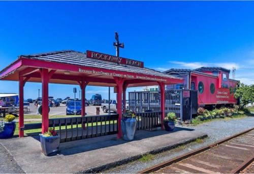 Sign for Rockaway Beach with a red building and a cross, surrounded by planters and a clear blue sky.