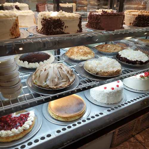 A display case filled with various cakes, including chocolate, fruit, and cream varieties, all beautifully presented.