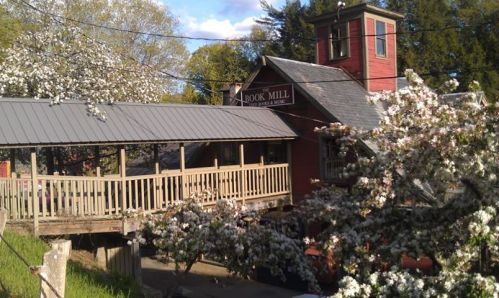 A red mill building surrounded by blooming trees and a wooden deck, set against a clear blue sky.