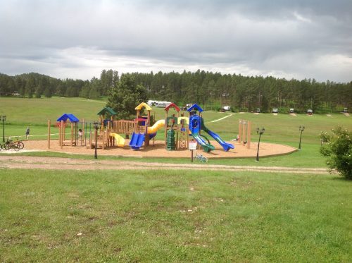 A colorful playground with slides and climbing structures, set in a grassy area under a cloudy sky.