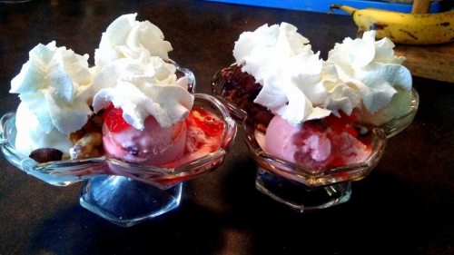 Two ice cream sundaes in glass bowls, topped with whipped cream, nuts, and strawberries.