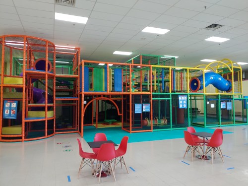 Colorful indoor play structure with slides and climbing areas, surrounded by tables and chairs in a spacious room.