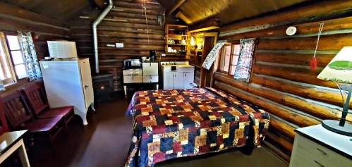 Cozy log cabin interior featuring a bed, kitchenette, and rustic decor with wooden walls and a warm atmosphere.